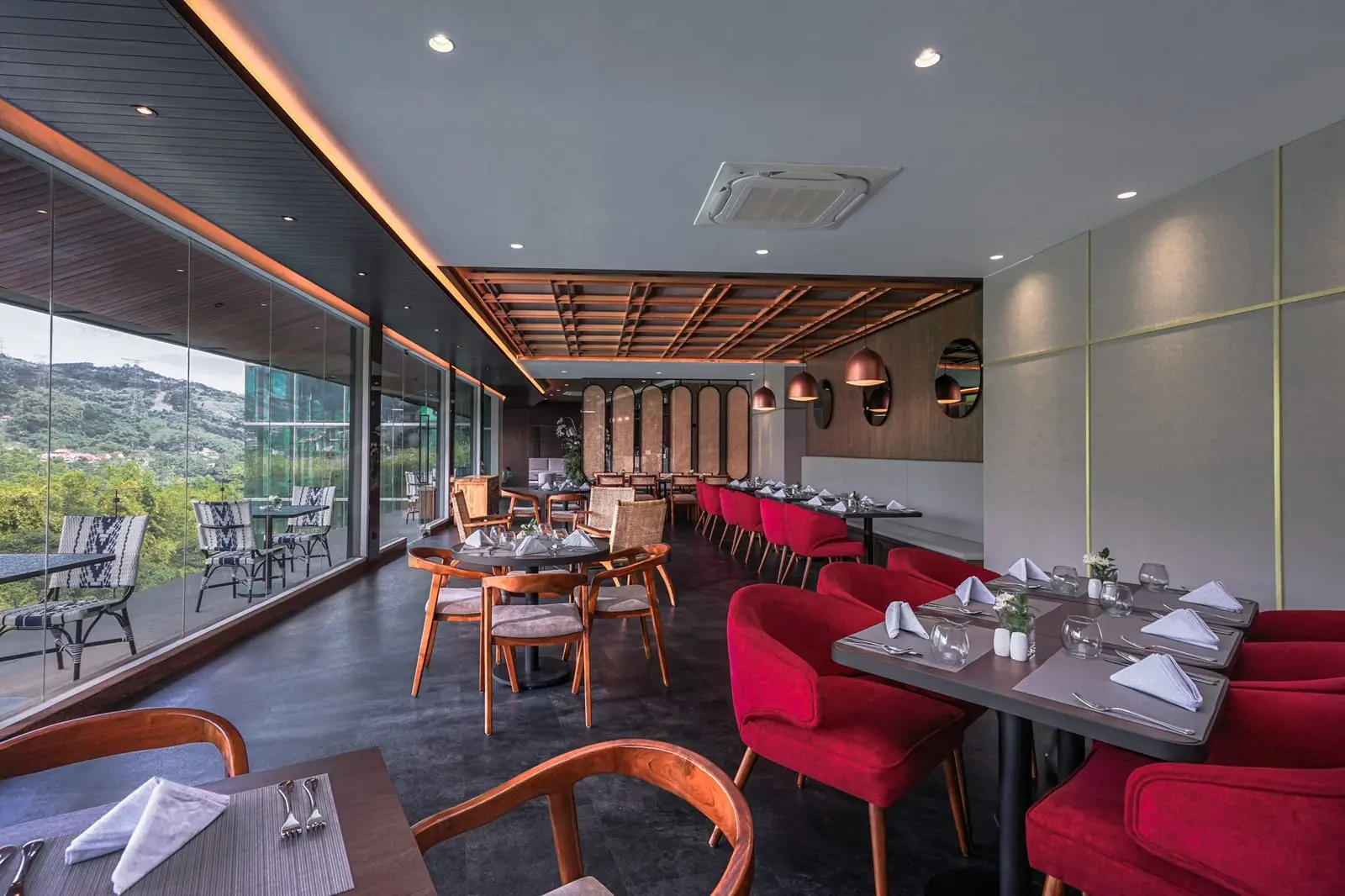 Spacious bar and lounge at Forest Hills Hotel Ciwidey with elegant red chairs, large windows overlooking the hills, and a cozy dining setup.